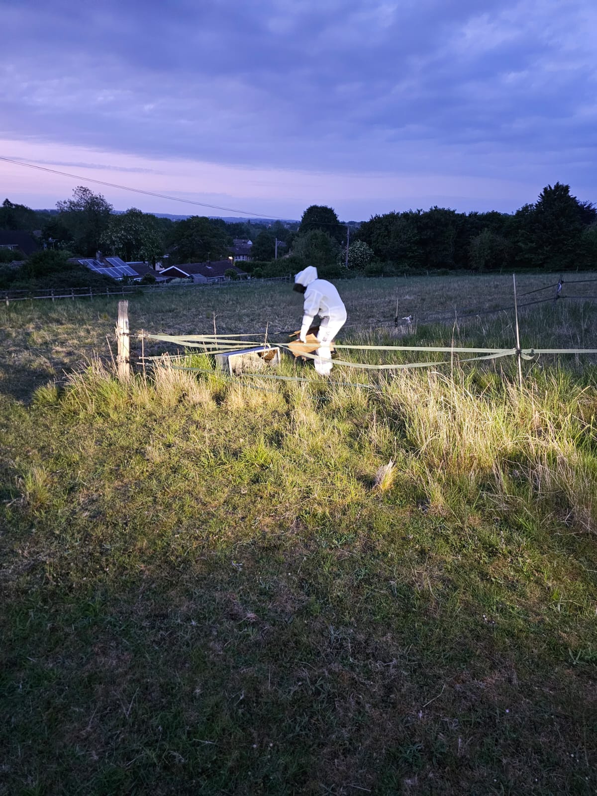 Adam in a white protective suit at work in a field at dusk